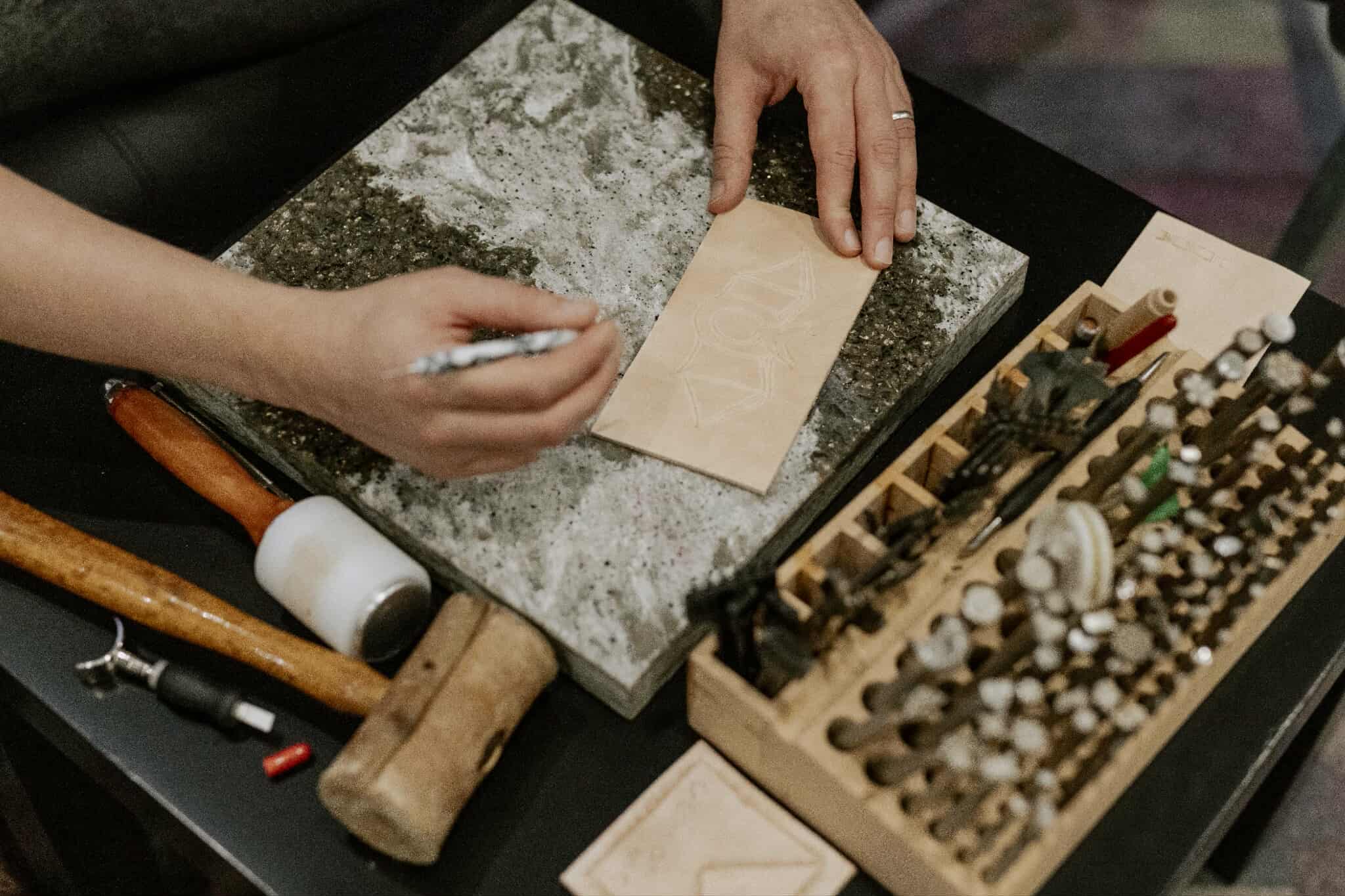 Person working with tools on a table with various items including a hammer and a box of stamps.